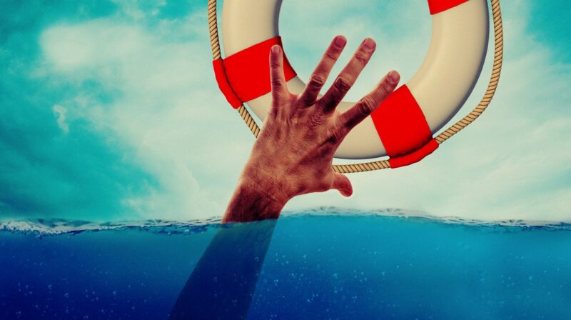 A hand reaches from under the water to grab a life preserver.