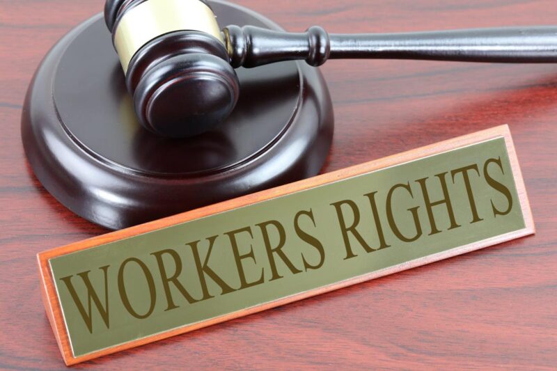 A gavel rests on a wooden desk. A plaque reading "workers rights" sits in front of it.