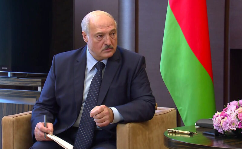 President Lukashenko. He sits, as if mid-debate or interview, next to a Belarusian flag.