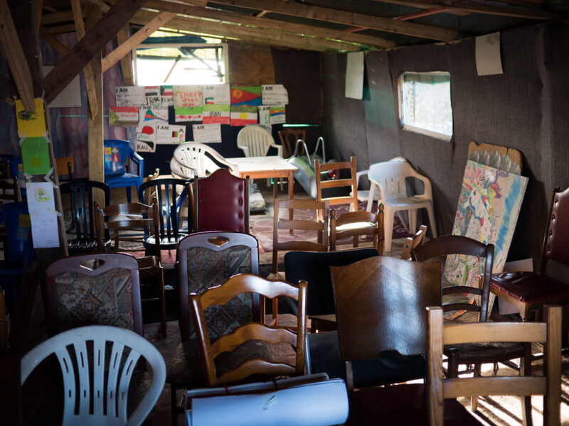 A classroom in the Calais migrant camp, in 2015. Many mismatched chairs are crammed together in a small, dark room.