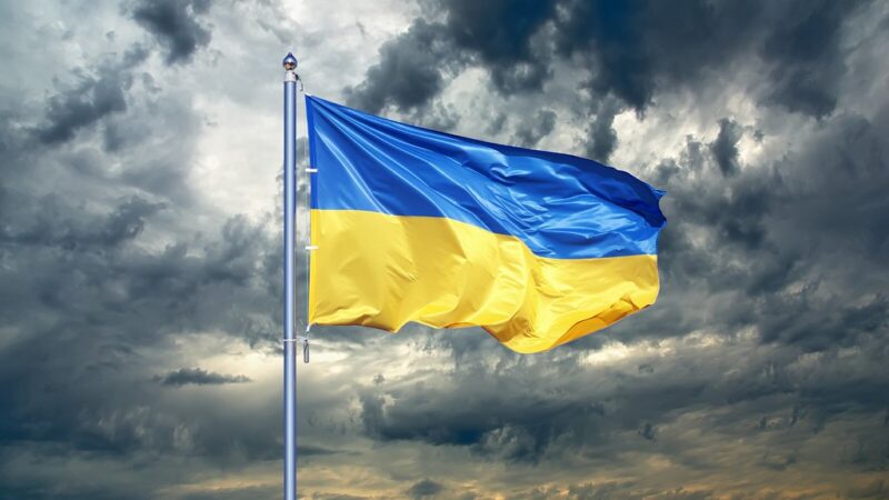 A Ukrainian flag ripples against a dark and cloudy sky.