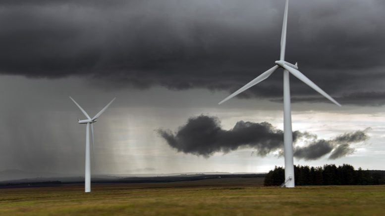 Windmills in an empty field. Dark gray clouds loom behind them.