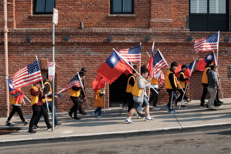 A parade marches up a San Francisco hill, wearing bright orange vests and carrying American and Taiwanese flags.