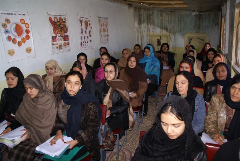 Women study nursing and health education at Afghanistan's Gawhar Shad University in 2007. The women are tightly packed in a long, narrow room. Four informational posters breaking down the face's sensory organs are visible on the wall.