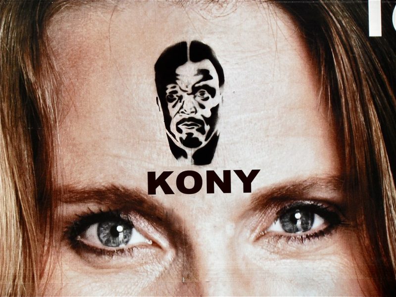 A blue-eyed white woman, photographed from the nose up, wears a stenciled tattoo of Kony's name and face on her forehead (evidently as part of Invisible Children's Cover the Night initiative, which directed supporters to "raise awareness" in similar fashion).