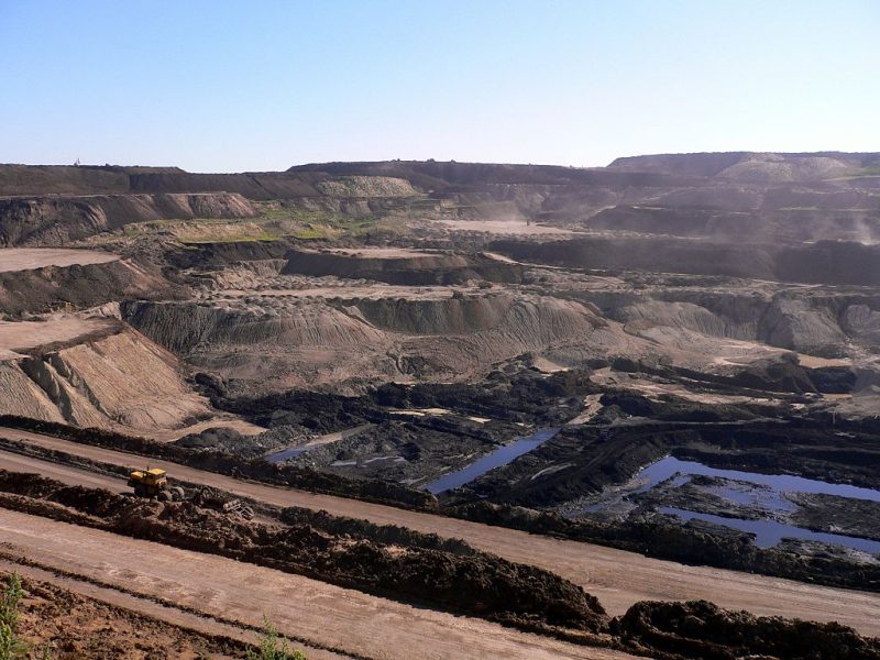 A coal mine in Hailar, Inner Mongolia, China. Water pools at the bottom of a large pit, broken into bare and shallow steps. A yellow machine at the bottom appears to be clearing more dirt.