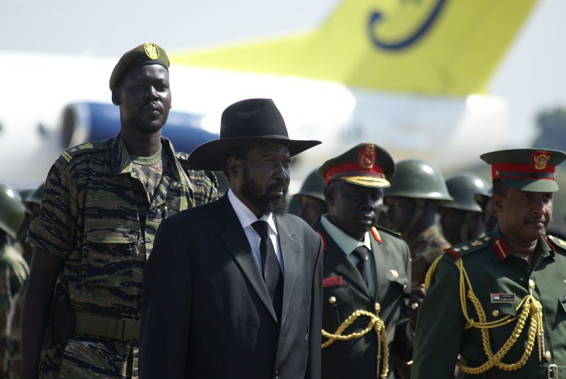 Kiir, in his iconic black Stetson and a plain black suit, stands in a crowd of decorated South Sudanian soldiers as he waits to receive former leader Omar al Bashir in 2011.