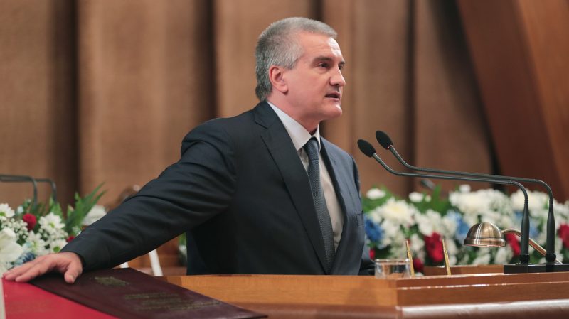 Sergei Aksyonov, photographed at his inauguration in 2019. He stands at a lectern, backed by rows of flowers.