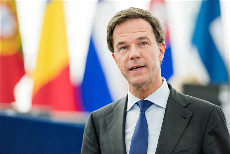 Mark Rutte, photographed in front of a row of flags.