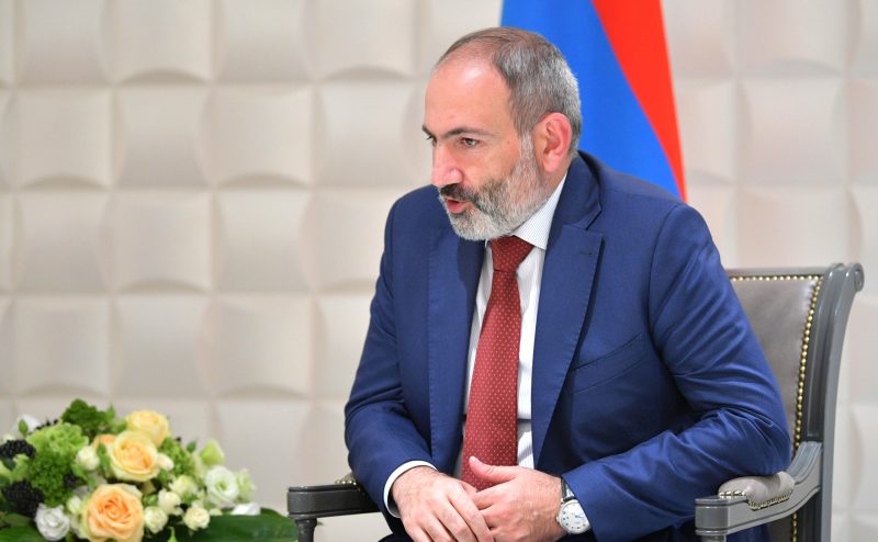 Prime Minister Nikol Pashinyan, photographed in 2019 at a discussion. An Armenian flag is standing furled behind him.