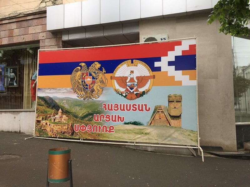 Armenian propaganda poster in occupied Khankendi, Nagorno Karabakh, Azerbaijan. The poster features the flag of Nagorno-Karabakh above two seals and pictures of the region.