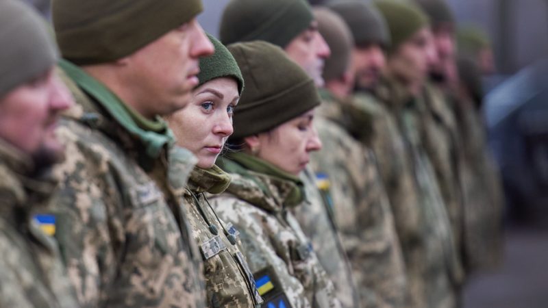 A female soldier peeks at the camera through a line of Ukrainian troops.
