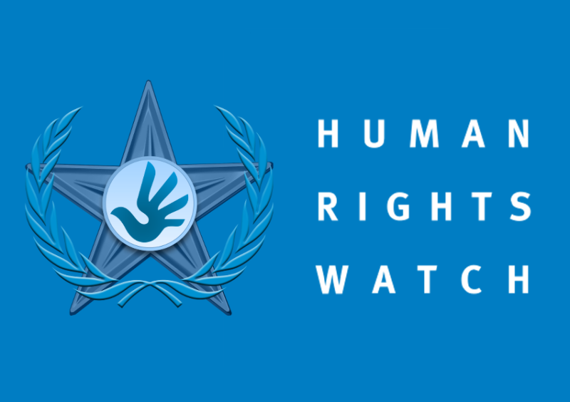 A blue banner with "HUMAN RIGHTS WATCH" written on the side in white block letters and the group's symbol, a reaching hand drawn to look like a dove, in a star and surrounded by an olive wreath.