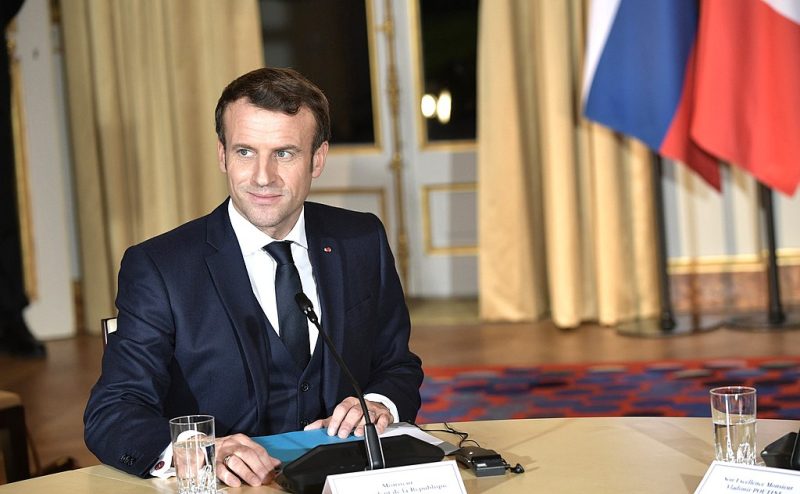 President Emmanuel Macron, photographed at a desk in 2019. The image is tilted slightly, giving it an offkilter feel.