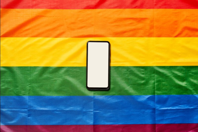 A phone displaying a blank screen sitting on a wrinkled rainbow flag.