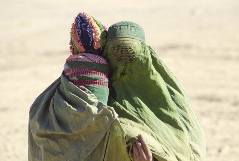 An Afghan woman and child at Roghani Refugee Camp in Chaman, a Pakistani border town. Both wear expansive green coverings.